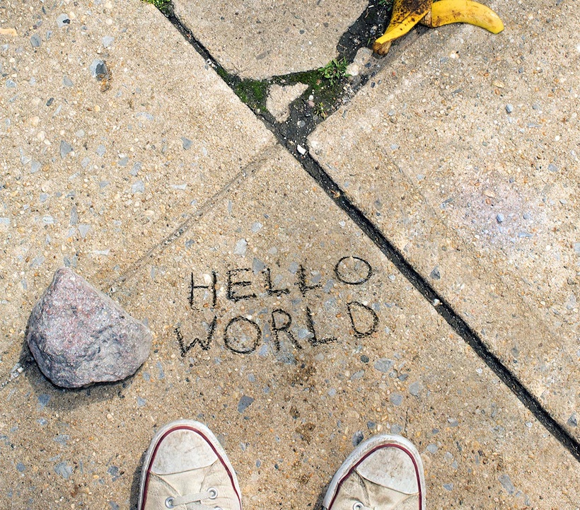hello world scratched into a sidewalk with shoes and a banana peel along the periphery