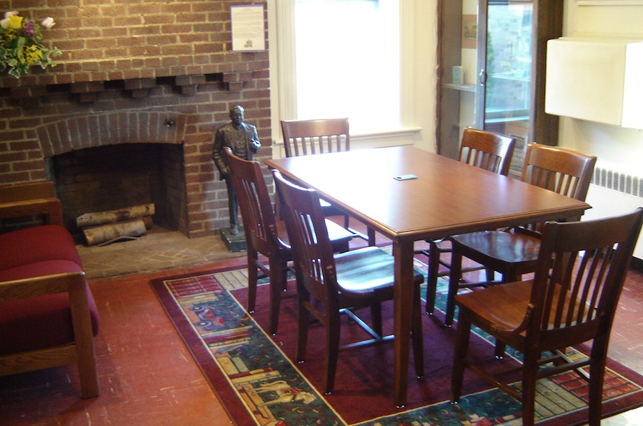 front room of library with table, chairs, fireplace, and bookshelf pattern carpeting